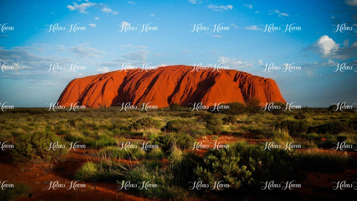 A stunning landscape view of Uluru (Ayers Rock) reveals its majestic, monolithic presence rising dramatically from the surrounding desert plains.